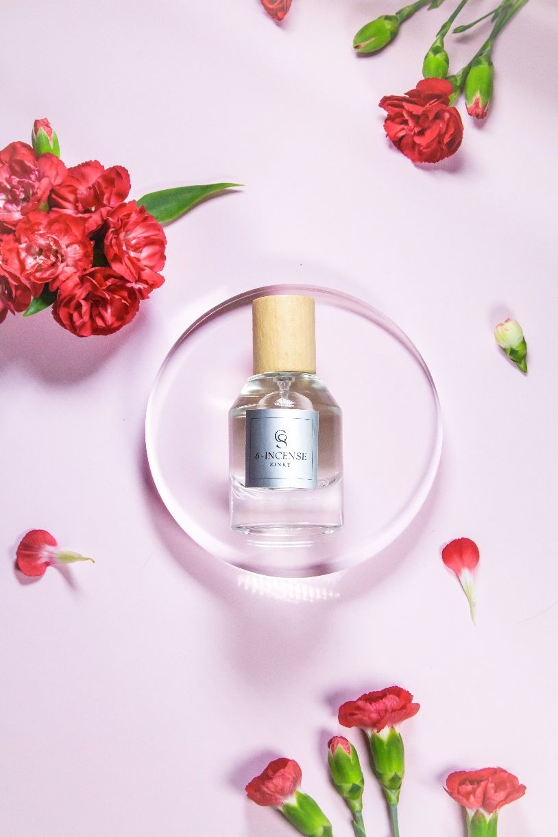 A bottle of perfume surrounded by red flowers\n\nDescription automatically generated